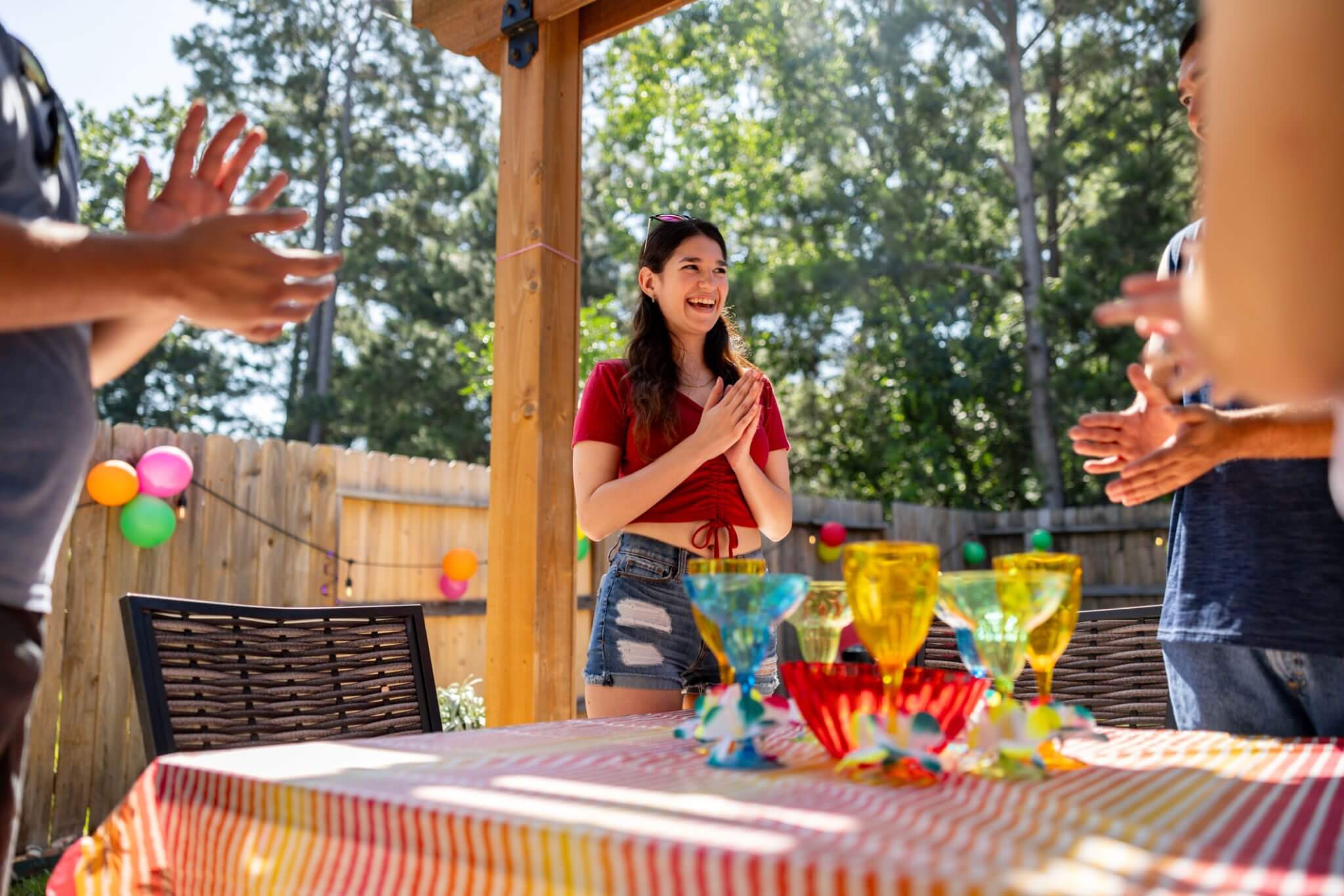 A woman clapping hands near trophies on a table outdoors.