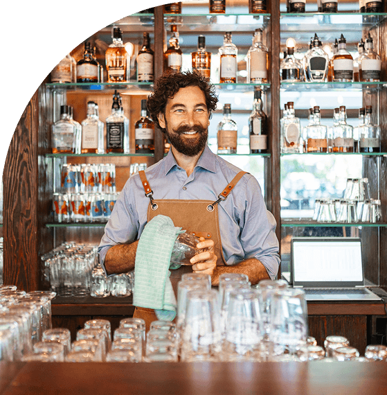 Bartender polishing glasses behind a well-stocked bar.