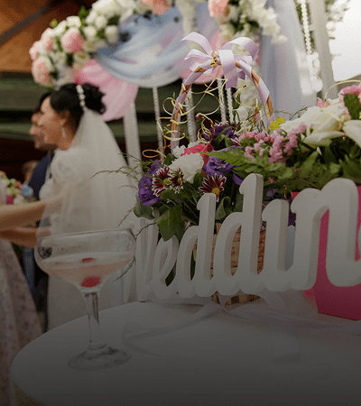 A bride at a wedding reception with floral decorations and a cocktail glass.