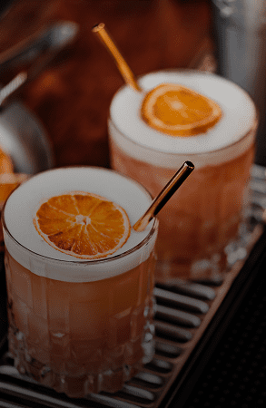 Two cocktails garnished with orange slices and black straws.