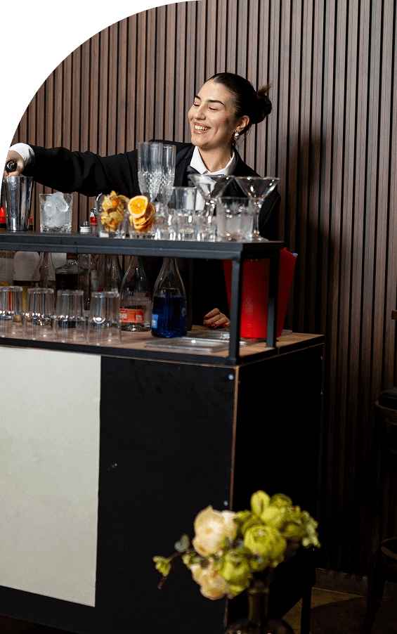 Bartender preparing cocktails behind a bar with various glasses and ingredients.