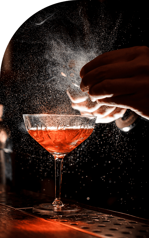 A hand sprinkles garnish over a red cocktail in a glass.