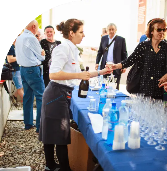 A server hands out drinks at an outdoor event with guests mingling.